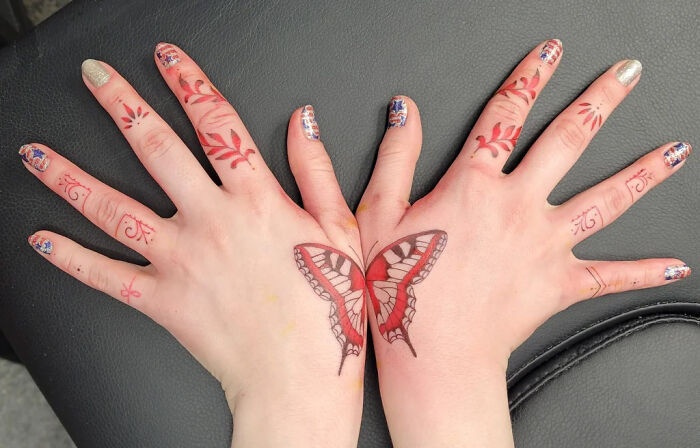 Small hand tattoos featuring a butterfly and red floral designs on the fingers.