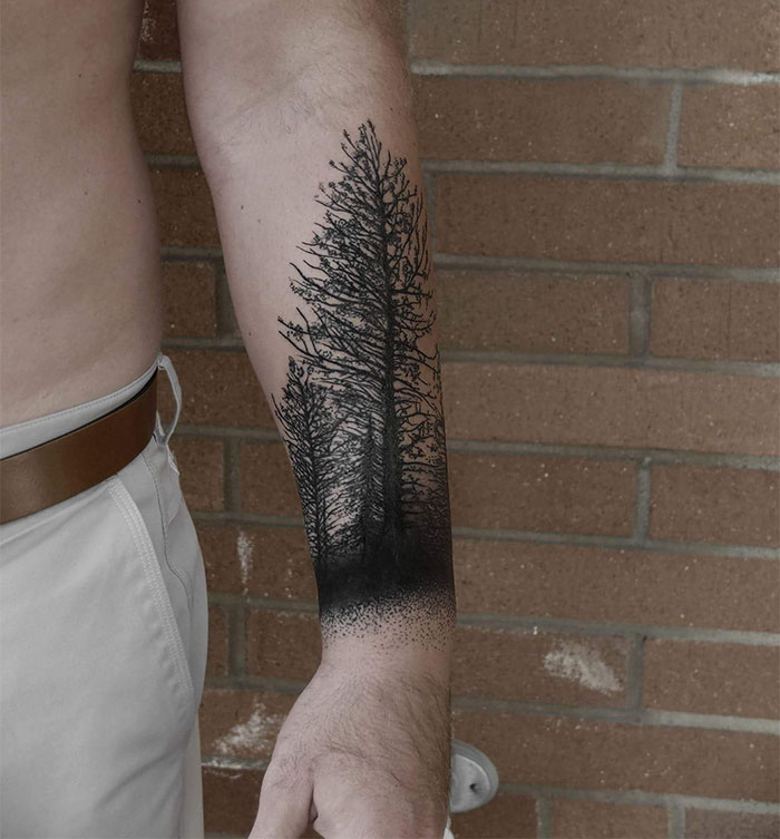 Majestic tree tattoo on forearm, showcasing intricate branches and shading against a brick wall background.