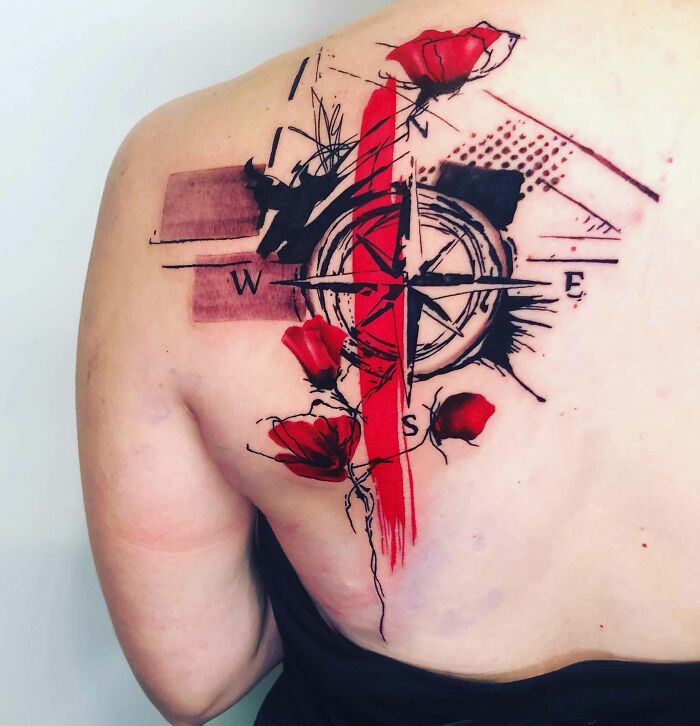 Trash polka tattoo with a compass and red flowers on a person's back.