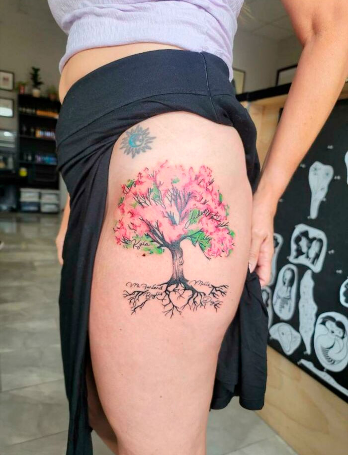 Tattoo of a vibrant tree with pink leaves on a person's thigh, celebrating the wonders of nature.