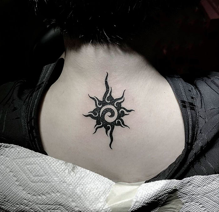 Tribal tattoo on back of neck, showcasing intricate black sun design.
