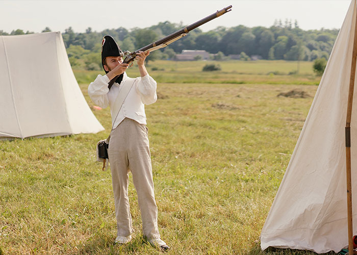 Man in historical military costume aiming musket outdoors, representing unique college courses in history reenactment study.