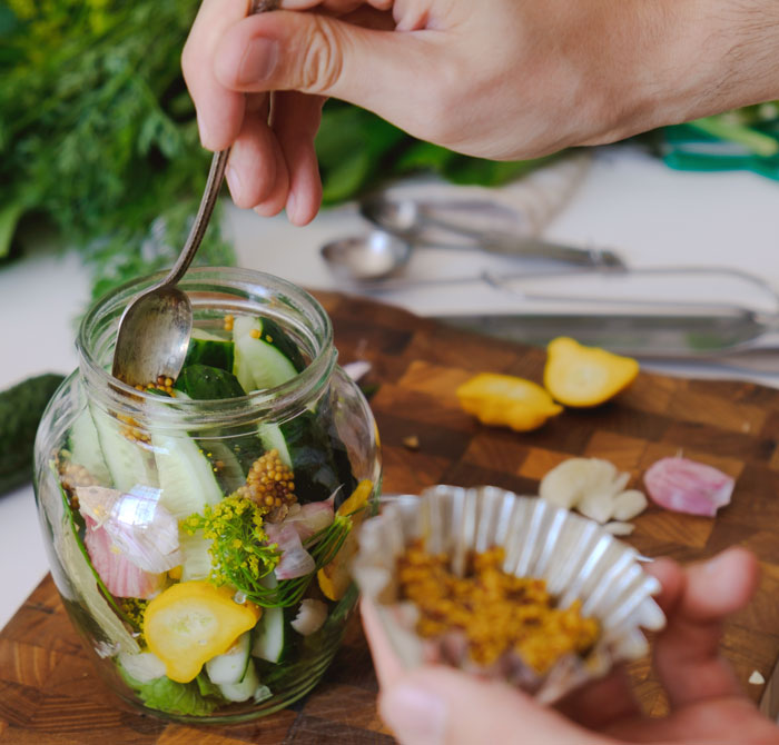 Preparing pickles in a jar with fresh vegetables and spices, illustrating unique college courses in culinary arts.