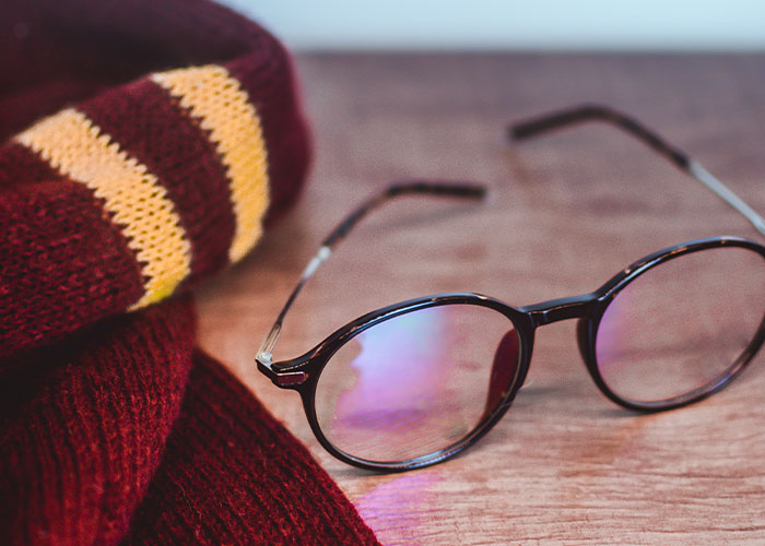 Round glasses with glare placed on a wooden surface next to a folded striped college scarf for unique college courses.