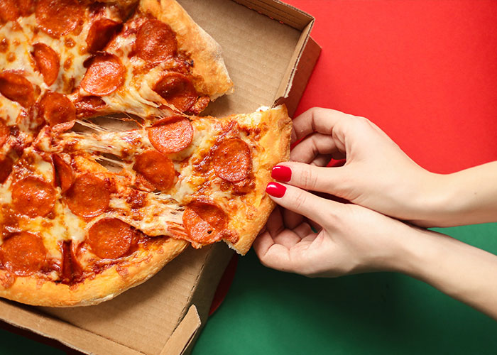 Person with red nail polish pulling a slice of pepperoni pizza from a box, illustrating unique college courses.