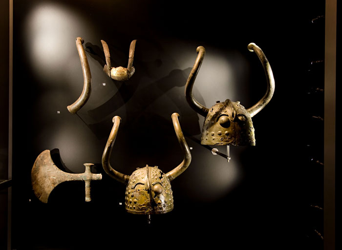 Ancient Viking helmets with horns and an axe displayed in a museum highlighting interesting Viking facts.