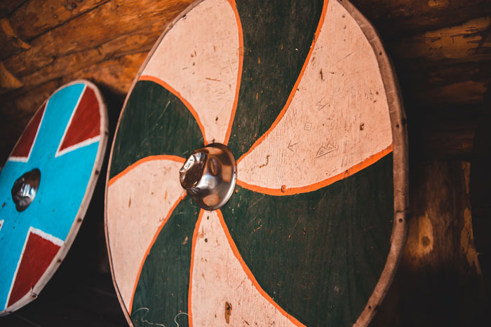 Round Viking shields with traditional painted designs resting against a wooden wall in a historic setting.