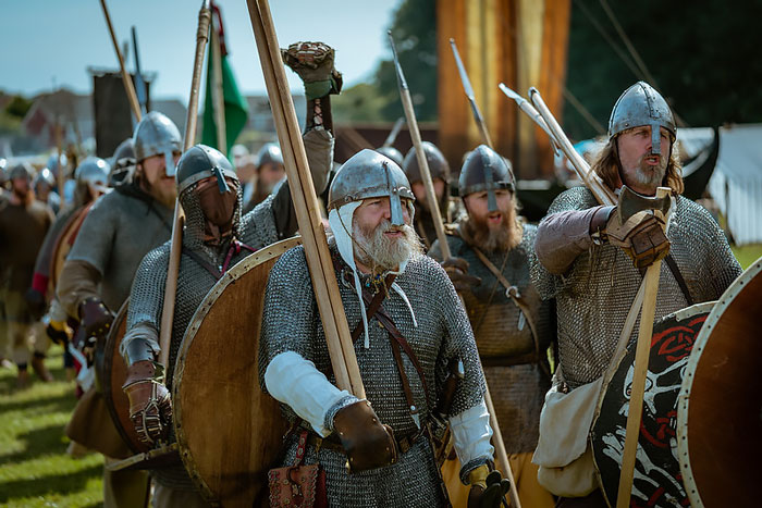 A group of Vikings in chainmail armor and helmets, holding spears and shields during a historical reenactment.