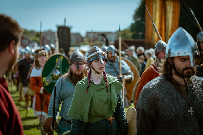 Group of people dressed as Vikings wearing helmets and armor during a historical Viking reenactment event outdoors.