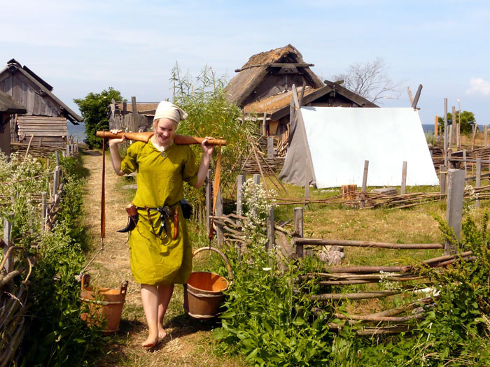 Woman in Viking-style dress carrying water buckets in a recreated Viking village showing daily life facts about Vikings.