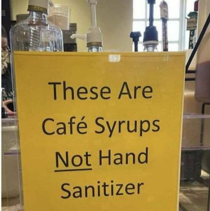 A coffee meme featuring a sign in a café that reads, "These Are Café Syrups Not Hand Sanitizer" in bold, black text on a bright yellow background. The sign is placed in front of syrup dispensers that might be mistaken for hand sanitizer pumps. The meme humorously points out the potential confusion between the two, especially in an era where hand sanitizer is commonly used.