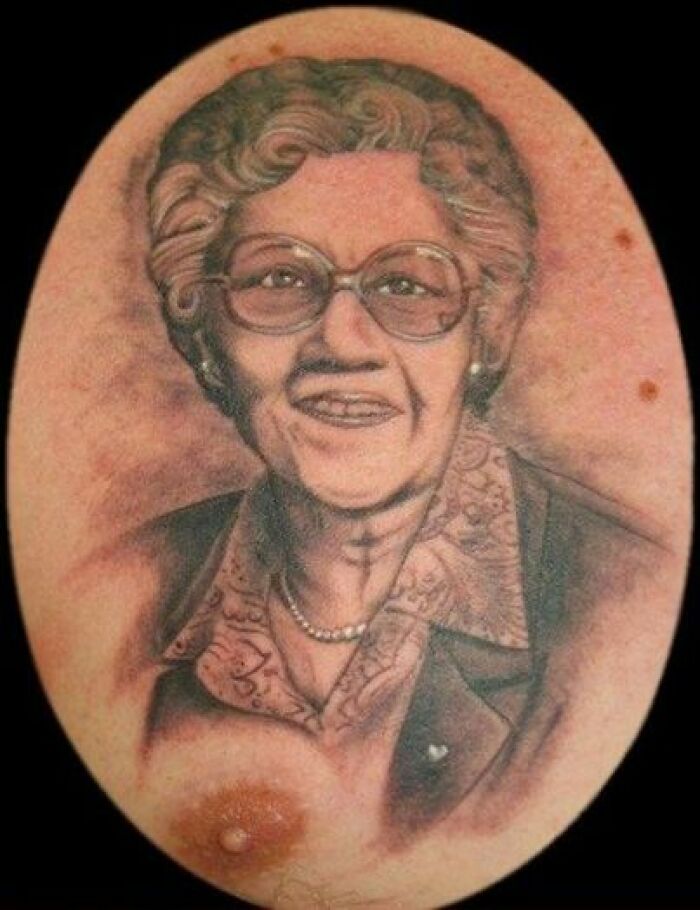 Portrait tattoo fail with older woman wearing glasses and a jacket.
