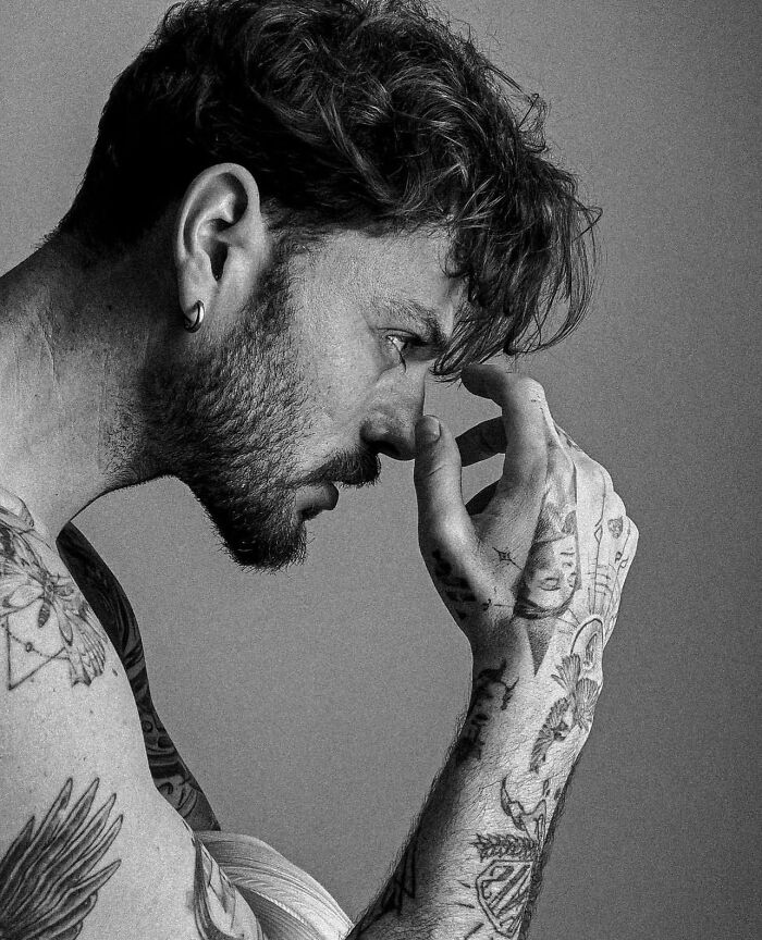 Profile of a tattooed man touching his face, showcasing geometric tattoo style on arms.