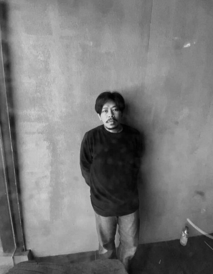 A tattoo artist in casual attire stands against a textured wall. Geometric tattoo style inspiration.