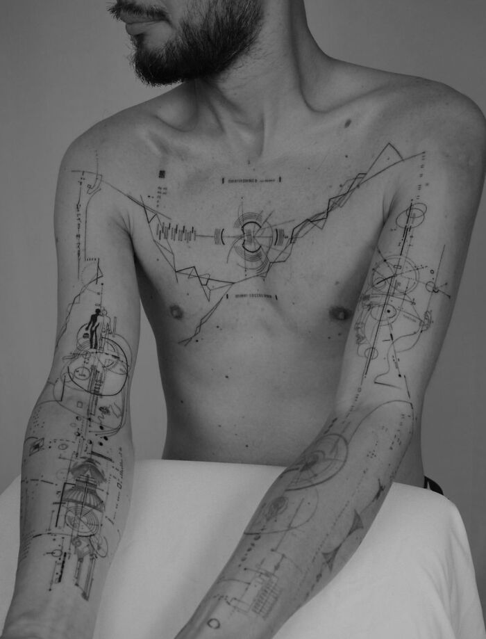 Man with geometric tattoos on chest and arms, featuring intricate patterns and lines in a minimalist black-and-white style.