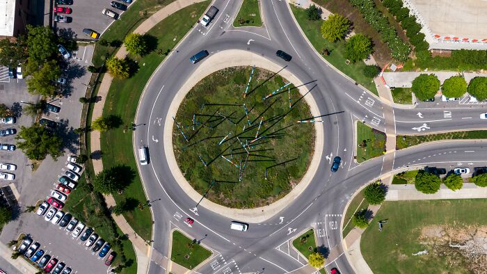 Aerial view of a roundabout with multiple cars navigating, illustrating chaotic human behavior and mistakes on the road.