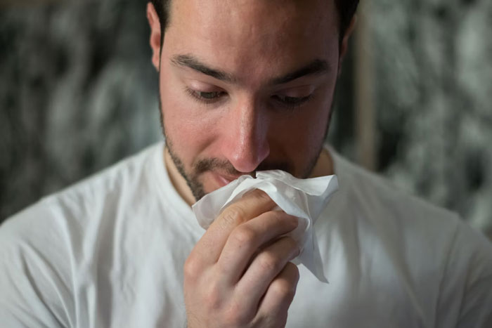 Man in a white shirt holding a tissue to his nose, illustrating annoying facts and urban legends people believe.
