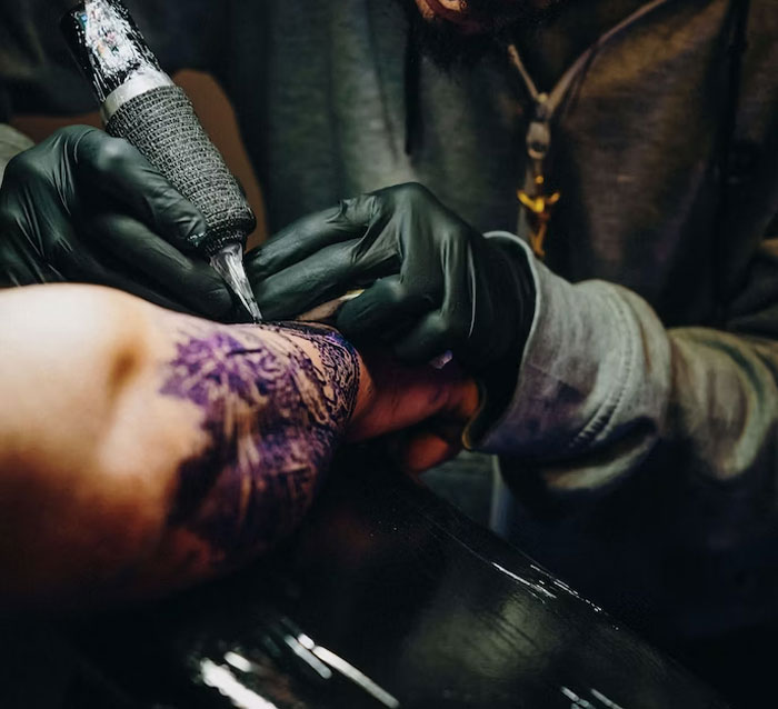 Tattoo artist in gloves working on a detailed design on a client's arm.