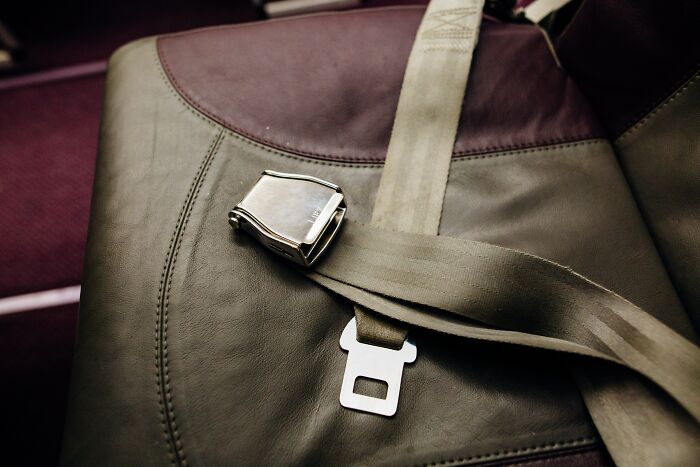Close-up of an airplane seatbelt on a brown leather seat, illustrating moments of human stupidity has no limits.