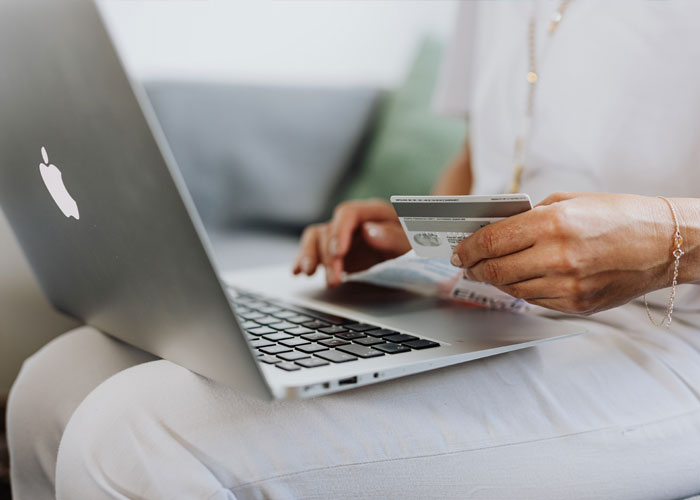 Woman holding credit card and using laptop, planning Hawaii trip despite ex-BF and family demands to skip vacation.