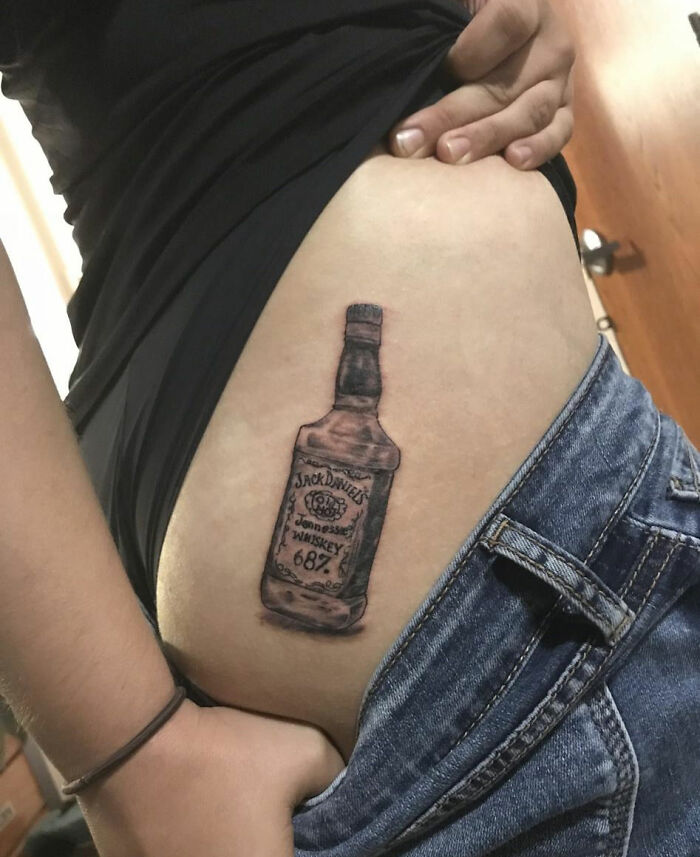Tattoo of a Jack Daniel's bottle on a person's hip, highlighted in a room setting.