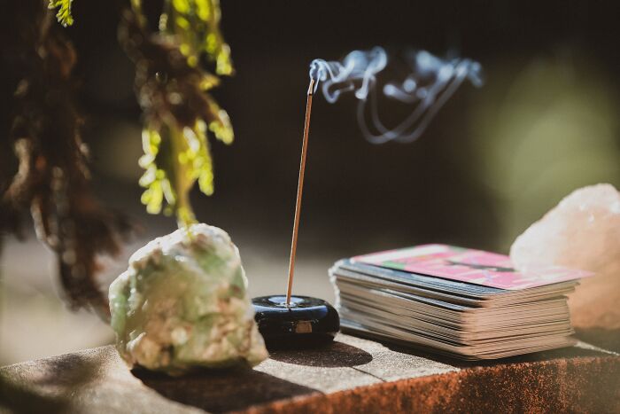 Incense stick burning beside crystals and tarot cards, symbolizing human stupidity and curious beliefs.