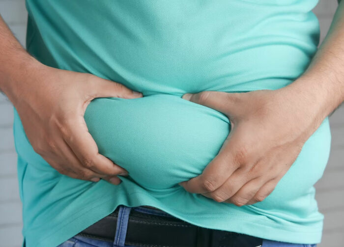 Close-up of a person squeezing belly fat in a turquoise shirt, illustrating common urban legends about weight and health myths.