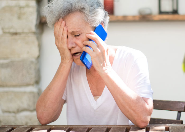 Older woman looking stressed while talking on the phone, relating to ex-BF and family demanding she skip Hawaii trip.