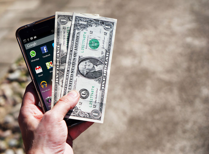 Hand holding a smartphone and two dollar bills outdoors representing man acting strange during first date concept.