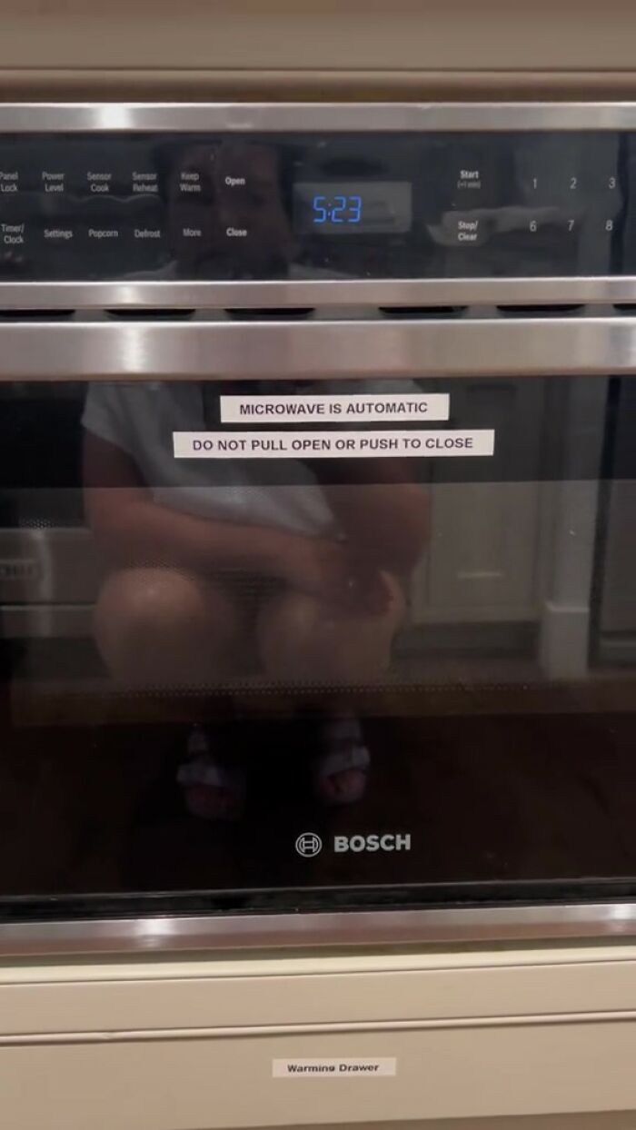 Microwave with printed rules sticker in an Airbnb kitchen emphasizing automatic function and strict usage instructions.