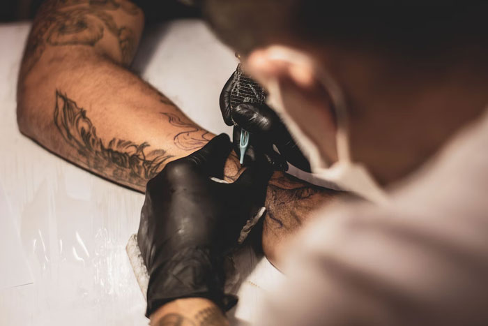 Tattoo artist with gloves applying a new tattoo on a person's arm in a close-up view.