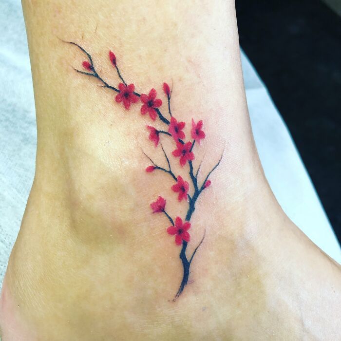 Floral ankle tattoo featuring red blossoms and black branches, showcasing tattoo inspiration and care.