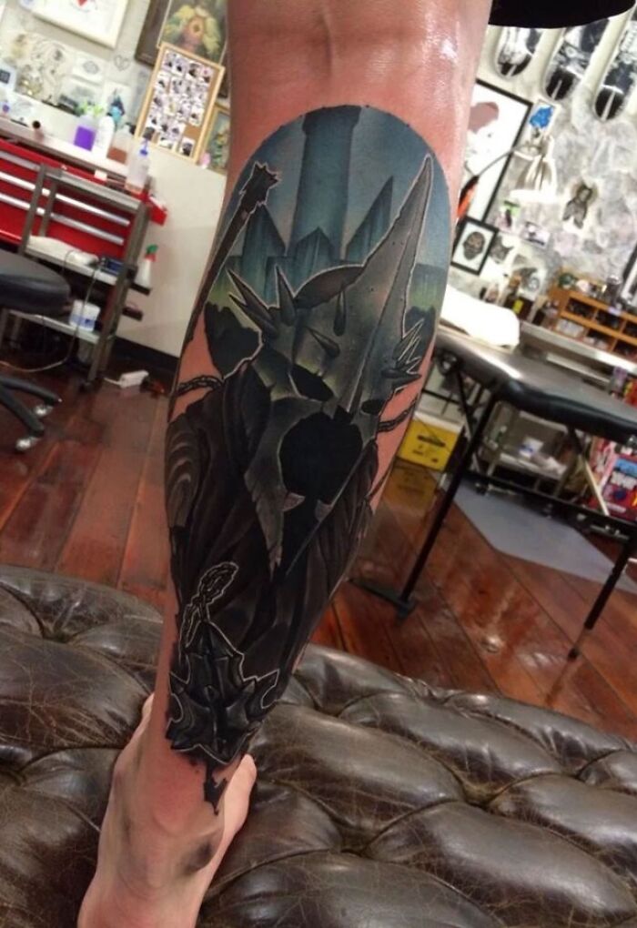 "Leg with Lord of the Rings tattoo depicting Sauron in a detailed and colorful design, inside a tattoo studio."