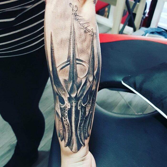 Forearm tattoo featuring a detailed Lord of the Rings design with Elvish script and dark armor elements.