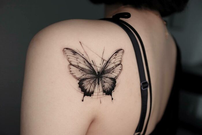 Butterfly tattoo on shoulder in black ink, showcasing detailed wing patterns.