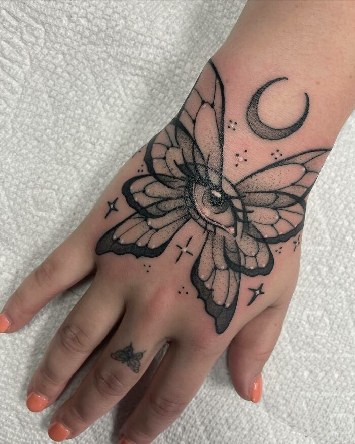 Butterfly tattoo with an eye and moon on hand, small butterfly on finger.