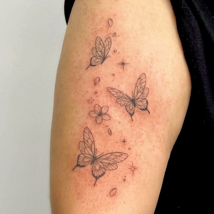 Black and white butterfly tattoos on an arm, featuring intricate design and small decorative elements.