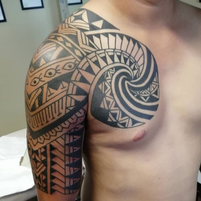 Tribal tattoo design on a man's shoulder and upper arm, featuring intricate geometric patterns.