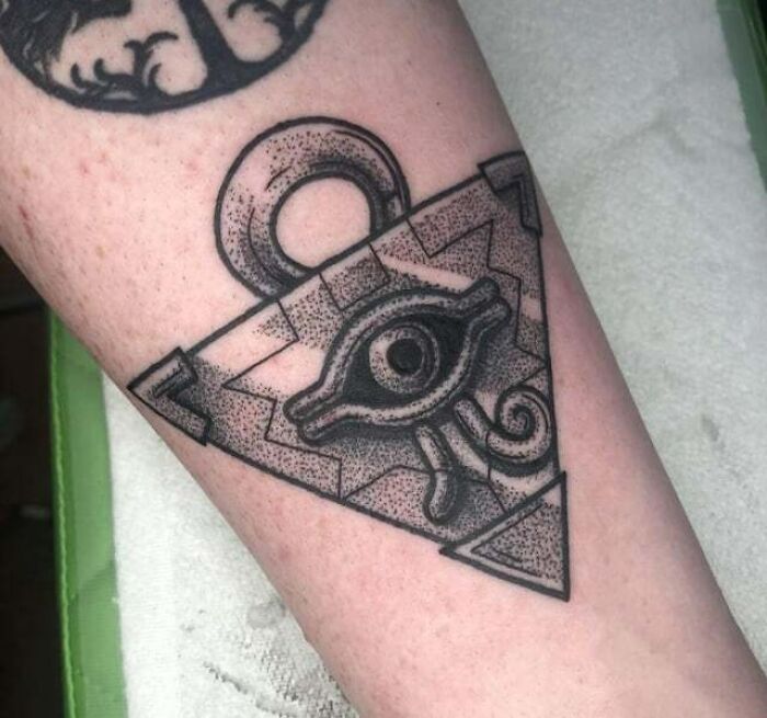 Anime tattoo featuring an artistic design resembling an eye symbol within a geometric shape on an arm.