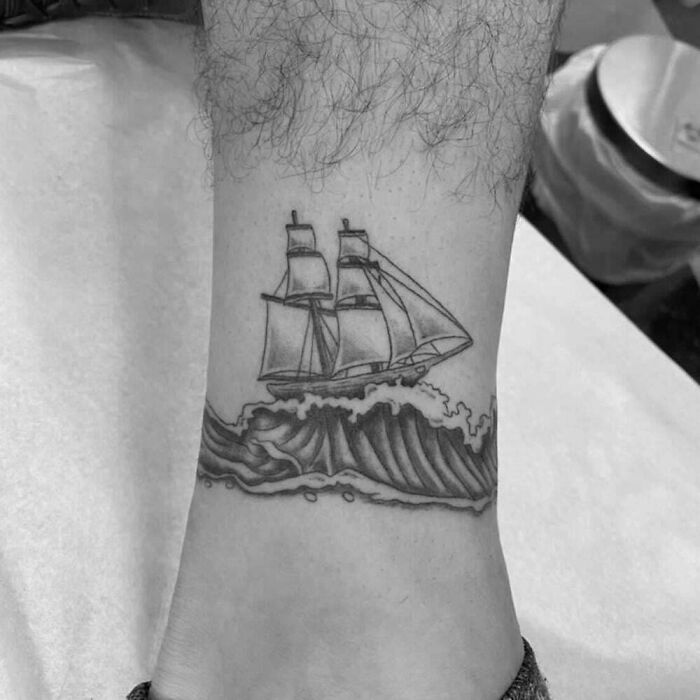 Ankle tattoo featuring a sailboat on waves.