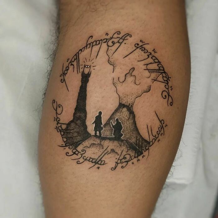 Tattoo featuring Lord of the Rings scene with Mount Doom and Elvish script on a person's leg.