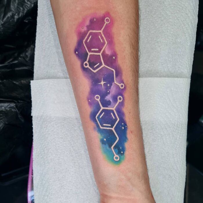 Colorful science tattoo featuring a molecule design on forearm, blending cosmic elements with chemistry art.