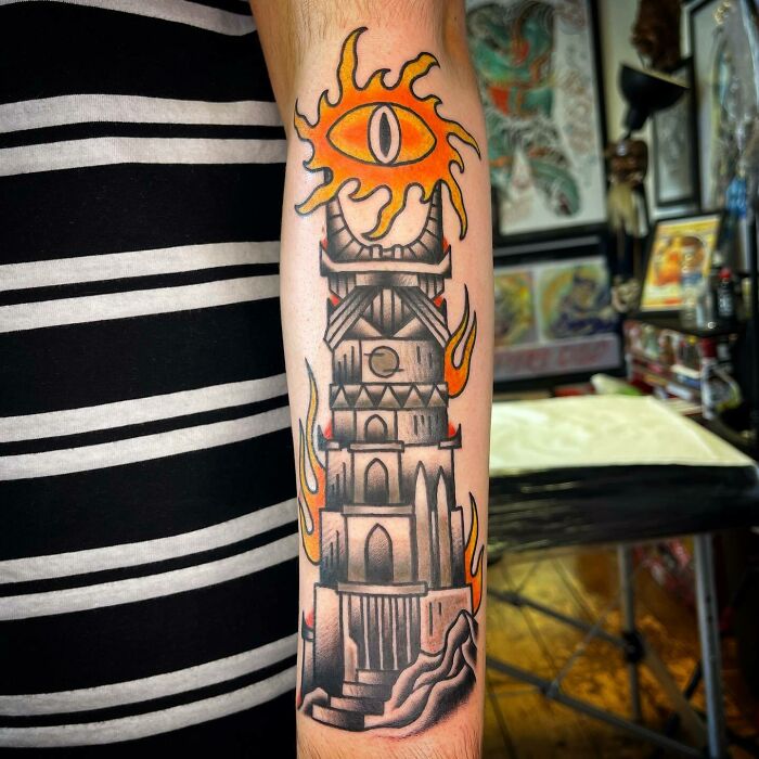 Lord of the Rings tattoo on forearm featuring a tower and flaming eye in a tattoo studio setting.