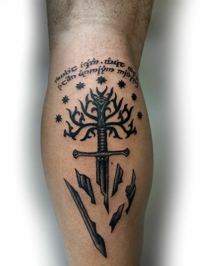 Lord of the Rings tattoo featuring a sword, tree, and Elvish script on a person's leg.