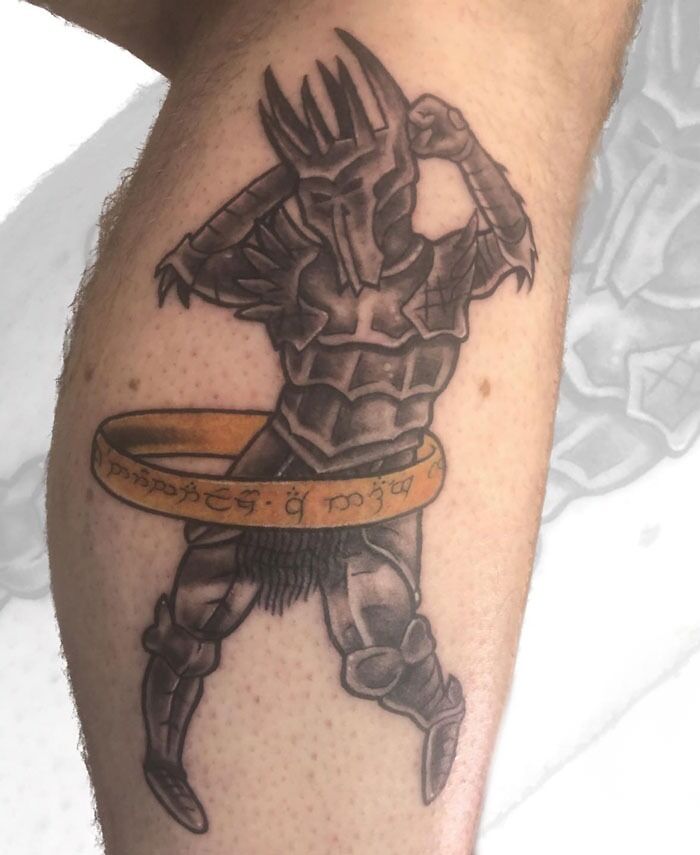 Tattoo of a dark armored figure with the One Ring from Lord of the Rings on a person's leg.