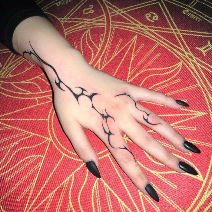 Intricate small hand tattoo with black nail design on a vibrant red background.