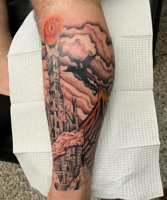 Lord of the Rings tattoo featuring a dark tower, fiery eye, and flying dragon on a leg.