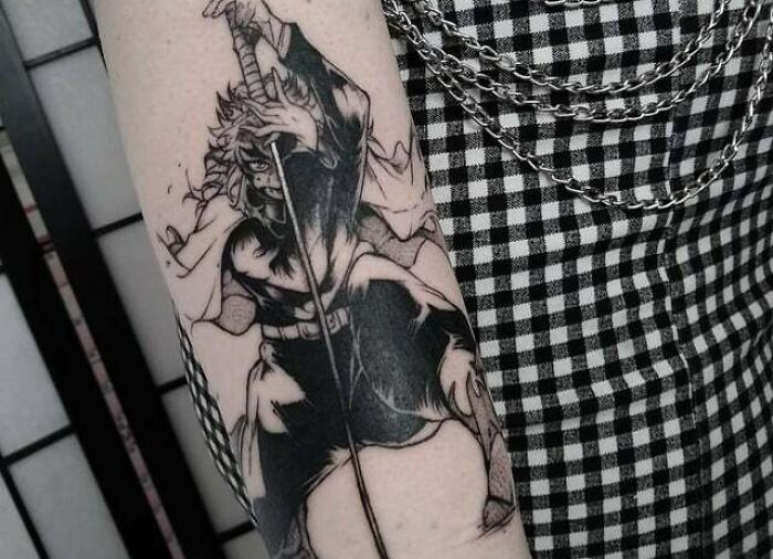 Anime tattoo depicting a character with a sword on an arm, showcasing intricate black and white design.
