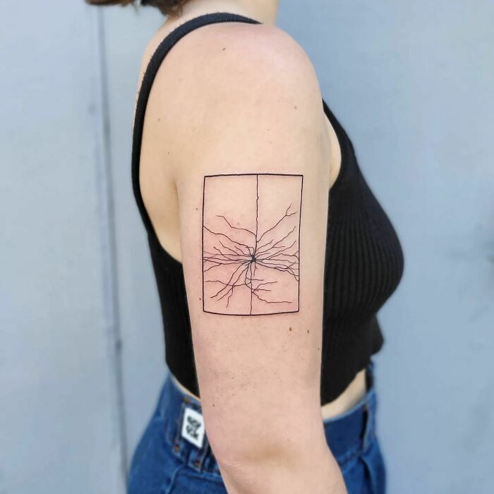 Minimalist science tattoo featuring a branch-like design, inked on a person's upper arm.