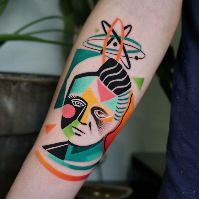 Colorful geometric science tattoo on forearm featuring an atomic symbol and abstract face.